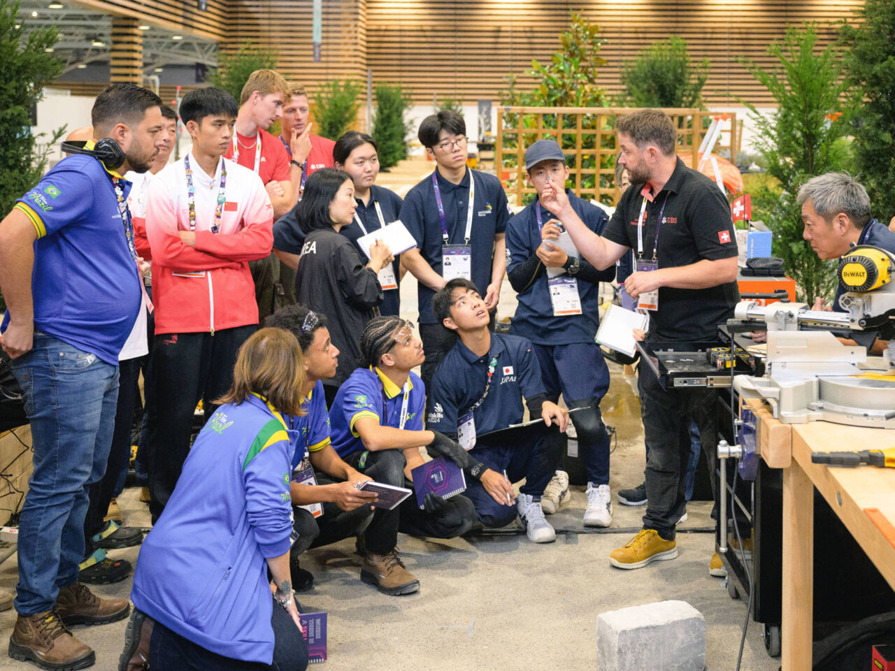 Competitors huddle around to listen to a Skill Expert during familiarization day at WorldSkills Lyon 2024.
