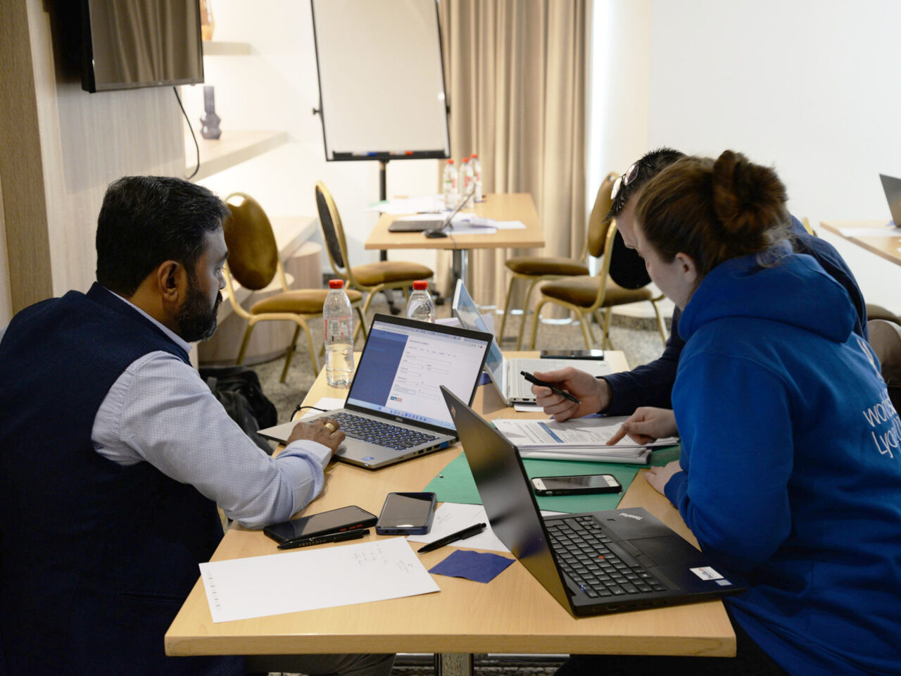 People sat at a desk looking at computers - one of the meetings taking place during the Competition Infrastructure Workshop in Lyon, France in March 2023.
