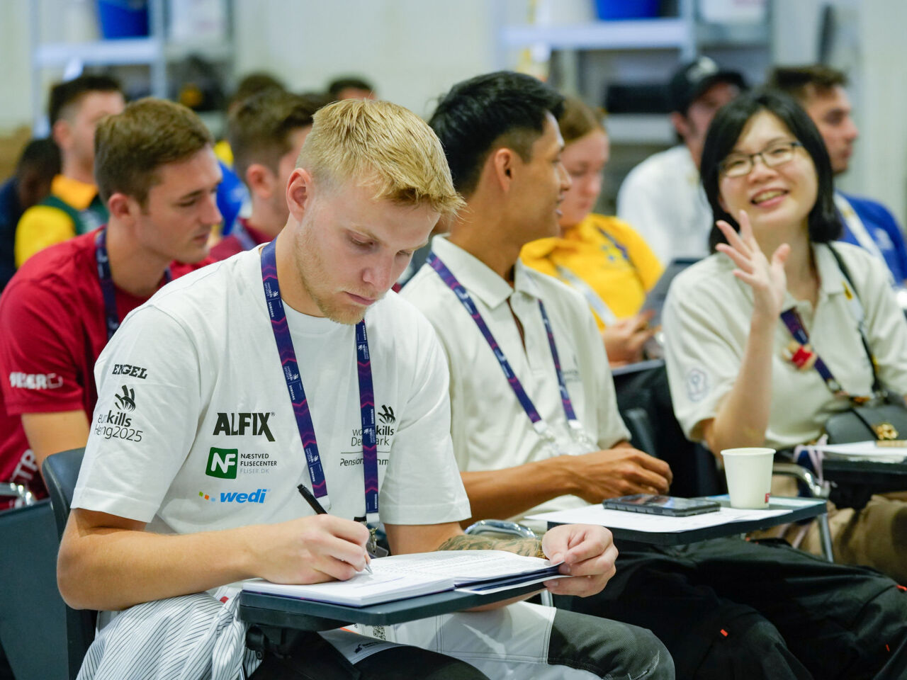 A Competitor from Denmark sat at a desk taking notes during familiarization day at WorldSkills Lyon 2024.
