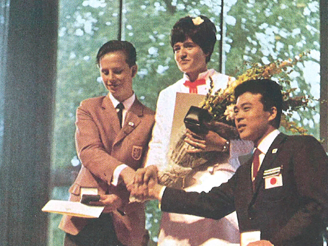 A colour photograph of Silvia Felix of Switzerland shaking hands with fellow winners at the podium after receiving the gold medal for Cabinetmaking at the 1968 competition in Bern.