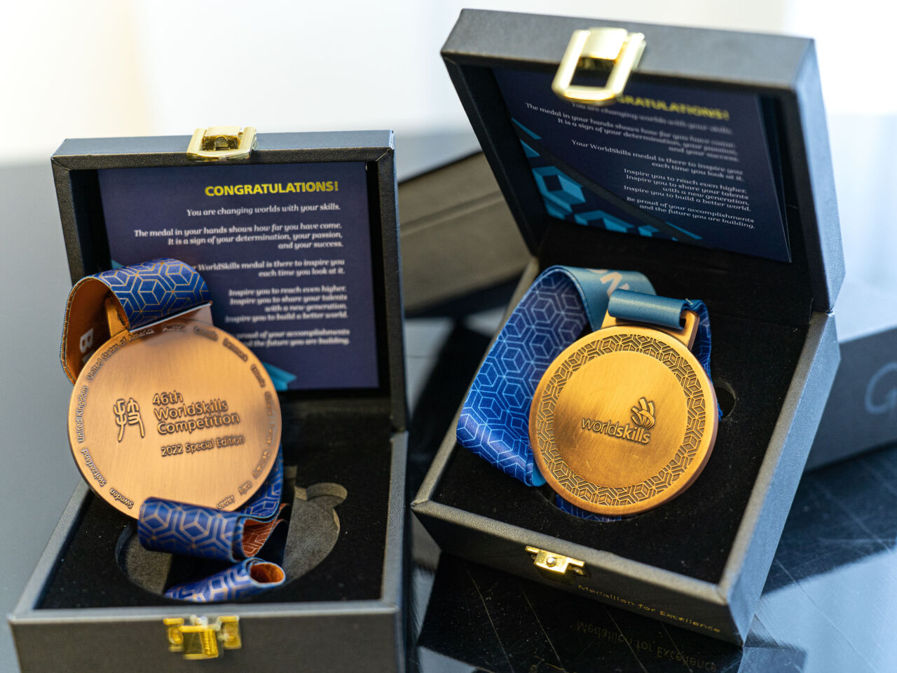 A close-up of two WorldSkills Competition 2022 Special Edition medals in their cases. The one on the left shows the front of the medal, while the one of the right shows the back.