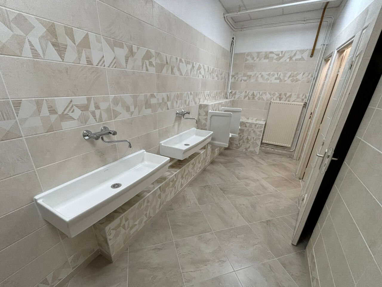 ewly renovated mixed-use washroom at BTP CFA Rhône showing modern white basins mounted on grey tiled walls with geometric patterns, chrome GROHE fixtures, and coordinating floor tiles.