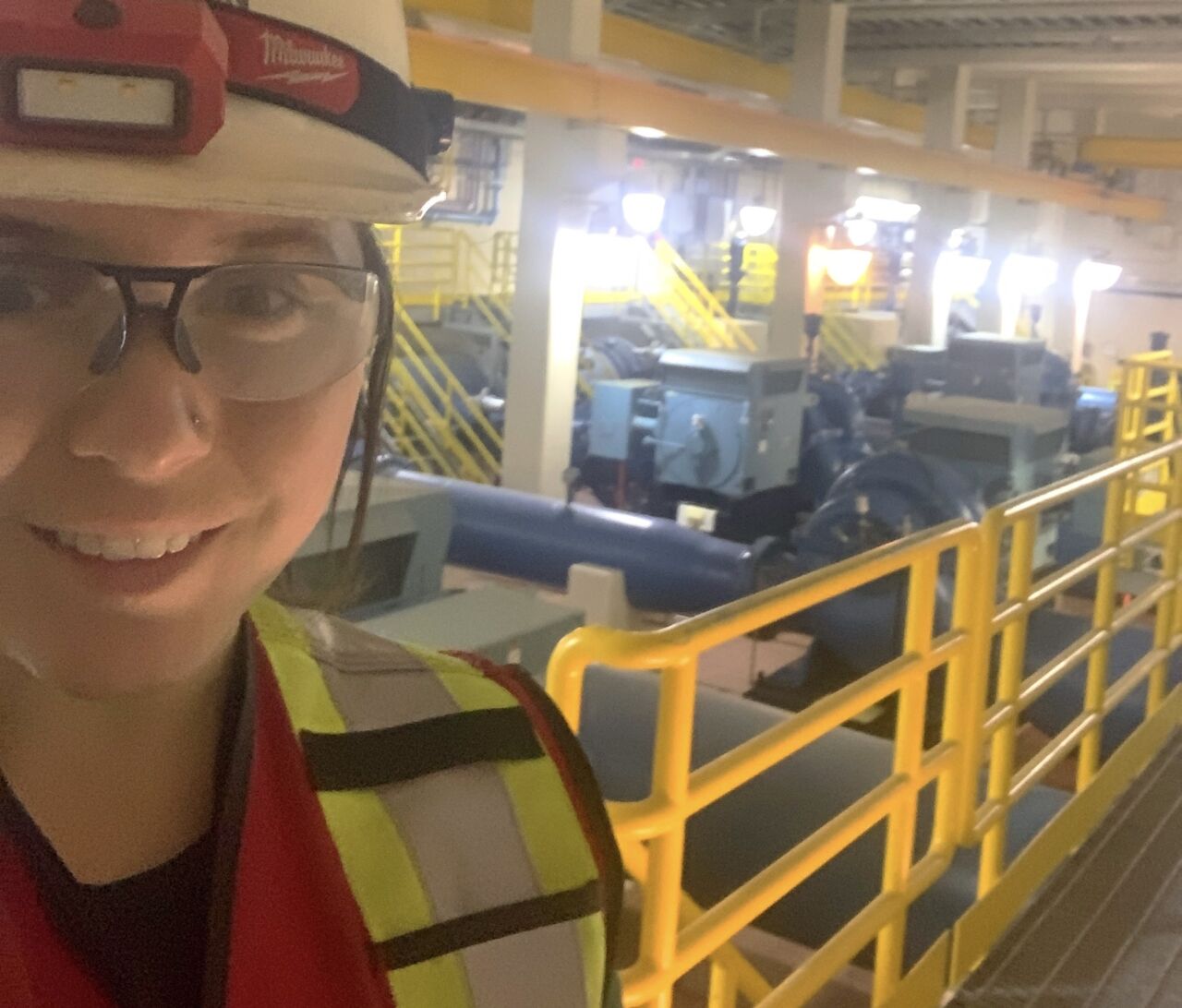 Deanna Reynolds, one of the few certified women Industrial Mechanic Millwrights in Canada, in a building with a large machine in the background.